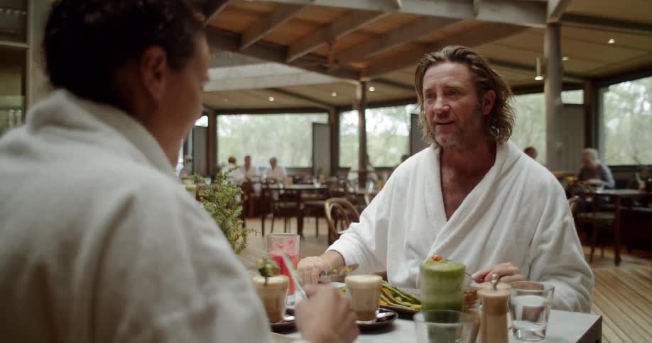 Two men sit at a table having a meal together wearing robes