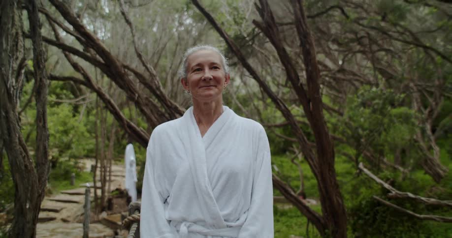 An elderly woman in a robe walks outside and looks around