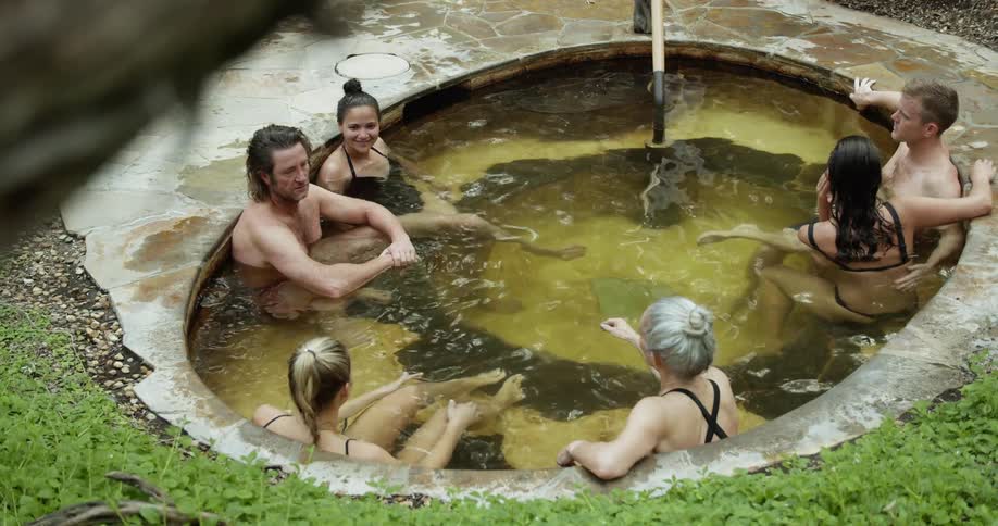 A group of people relaxing in a kind of thermal bath surrounded by bushes