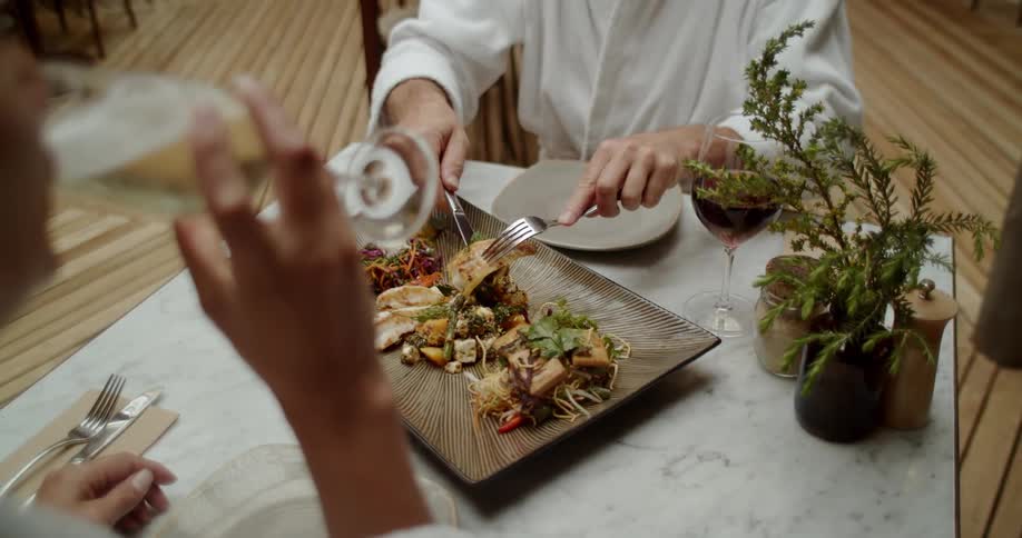 A couple sit at a table and eat dinner and drink wine