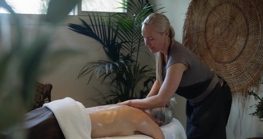 An elderly woman lies on a table as another woman massages her back