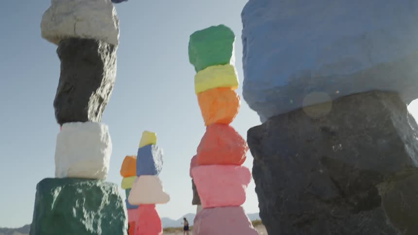 Two people walking in the desert near columns of colored stones