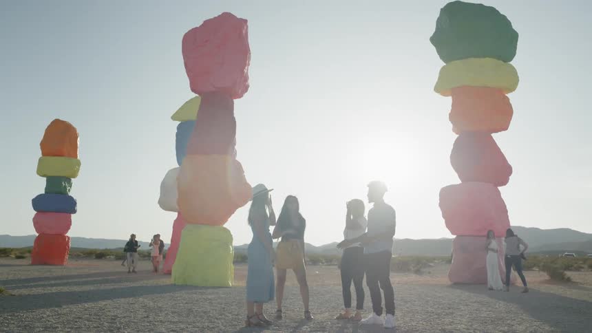 People standing and talking in the desert next to four large rock sculptures