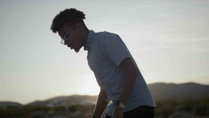 A young man kneeling before a stack of stones in the desert
