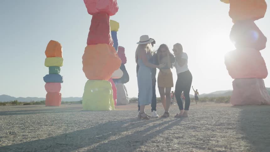A group of friends gathered under the painted rock art installation in the desert called seven magic mountains