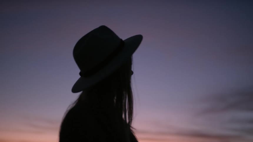 A womans shadow is standing outside wearing a hat
