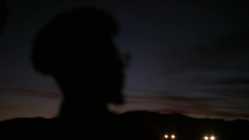 Black man wearing glasses looks ahead outdoors at dusk