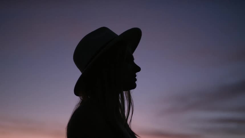 A woman in a hat standing outdoors during the sunset