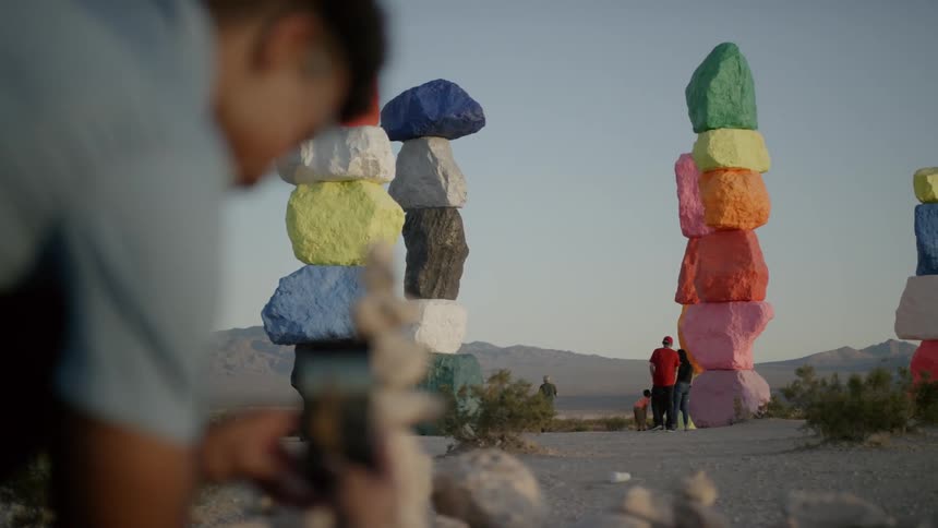A man using a phone to take a photograph of a family standing near a column of colored stones