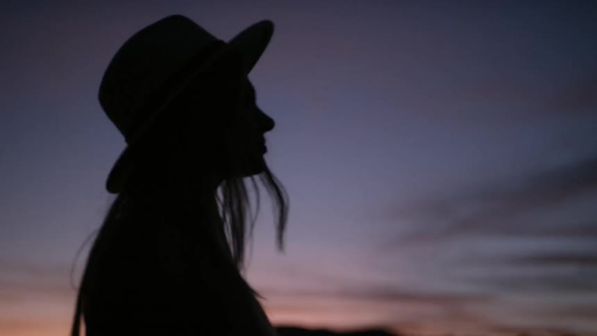 Silhouette of a young woman standing outside and looking across the landscape