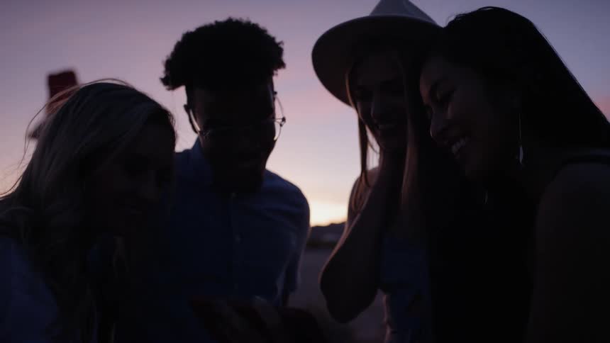 A young man and a group of young women gathered around in a circle looking at a smartphone