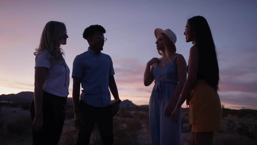 A young man and three young man standing together and talking in a desert at sunset