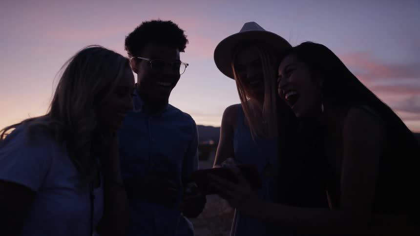 A group of people laugh together while standing outside with little sunlight