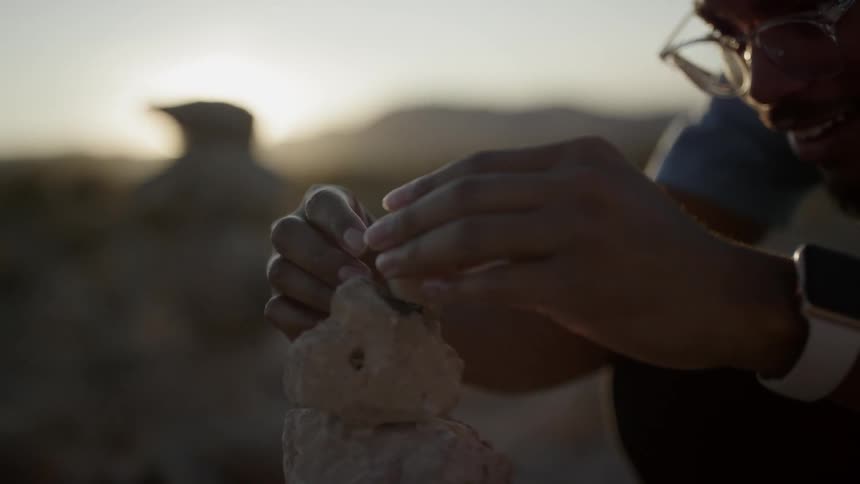 A man smiles as he tries to place and balance a stone on a stack of rocks