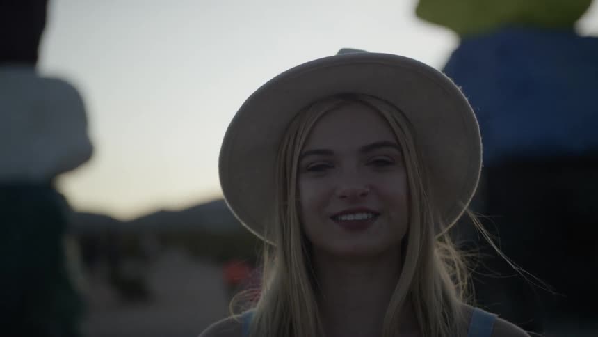 A young woman in a sun hat standing outdoors and smiling while looking into the camera