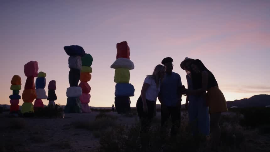 A group of people gathered together looking at smartphone in the desert at sunset