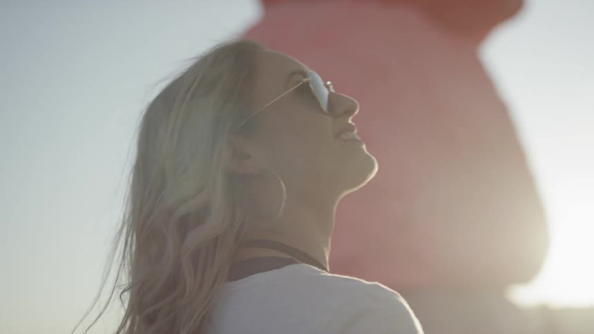 A woman with shades looking up at large colorful rock sculptures with the sky in the background