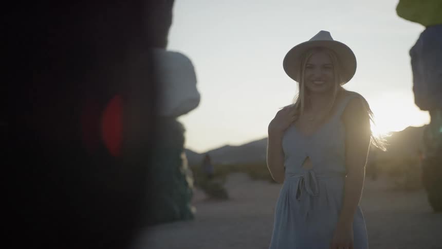 A woman in a sun hat smiles and poses for a picture while standing near colorful rock pillars