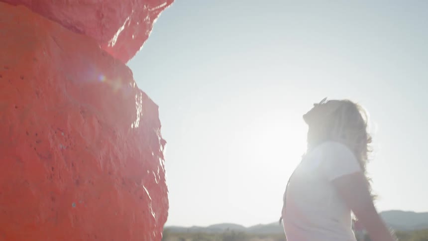 A young woman walks up to a large sculpture and pushes on it