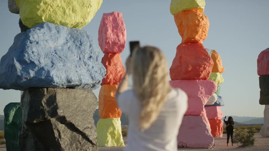 A woman using a smartphone to take pictures of a columns of colored stones in the desert