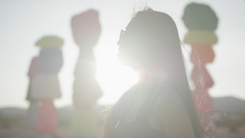 A woman stands in the sunny desert near the colorful seven magic mountains art installation