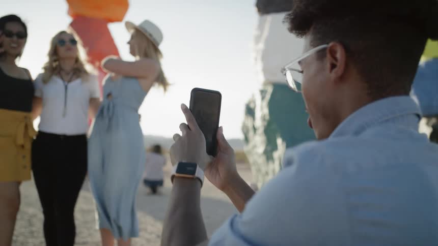 Three woman standing for a picture as a man takes a picture of them on his smart phone
