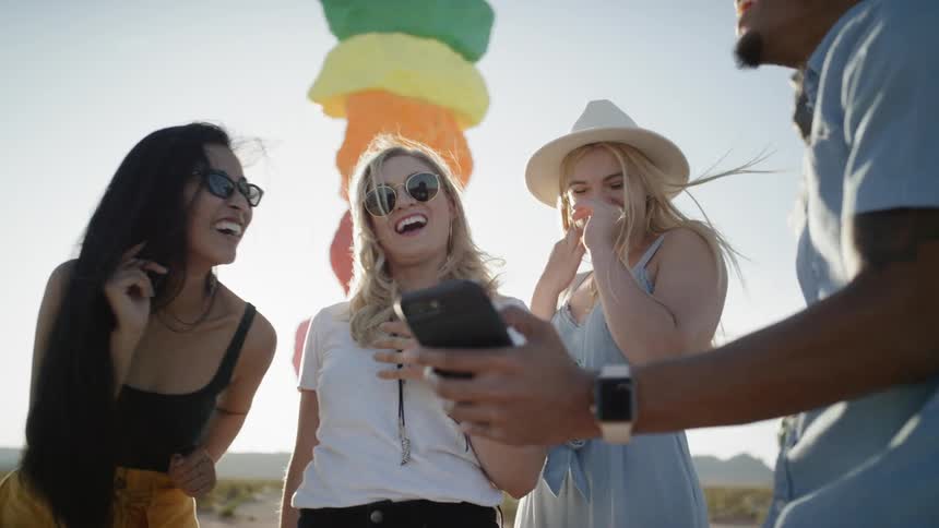 Revelers laugh together while one of them shows the rest something on his mobile phone