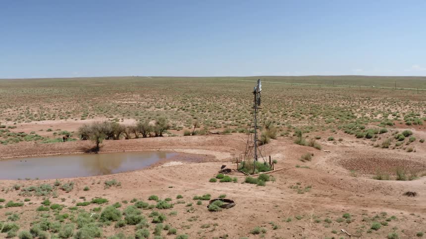 A windmill stands tall in the desert next to a small pond