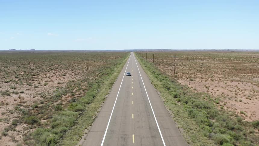 A car drives down an empty highway in the middle of a flat landscape