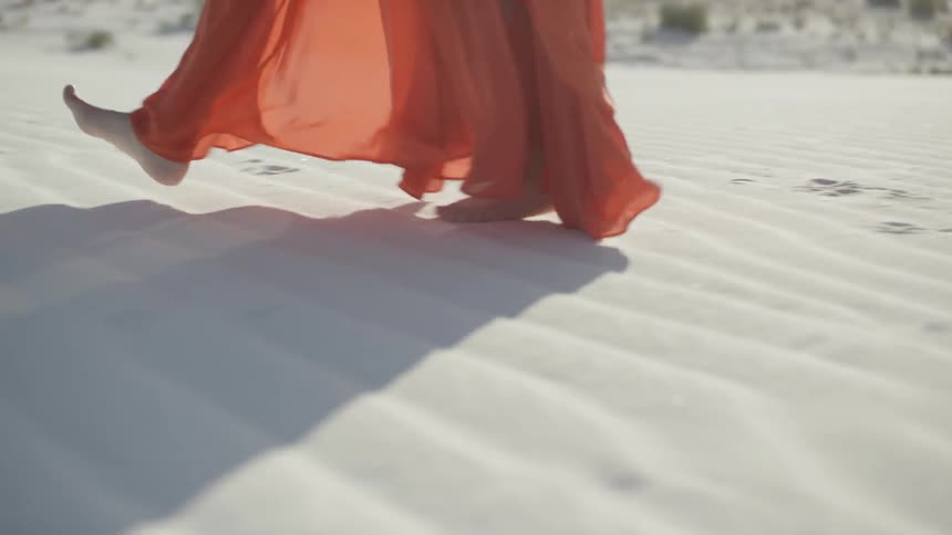 A woman walking on the desert sand with an orange dress