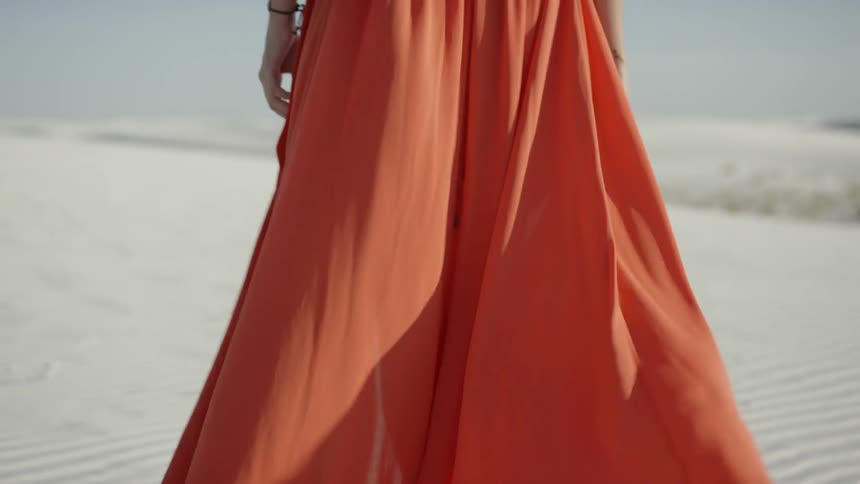 A woman in a full length dress walking on sand dunes looking out to the horizon
