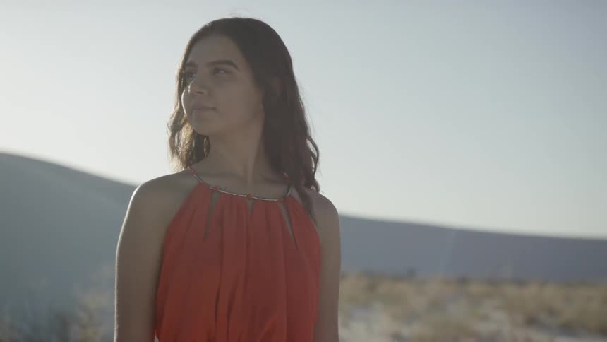 A woman dressed in red looks around at the desert on a sunny day