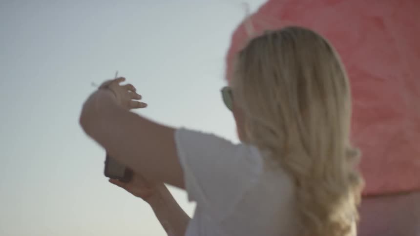 Blonde woman wearing sunglasses takes picture of colorful stone pillars at sunset
