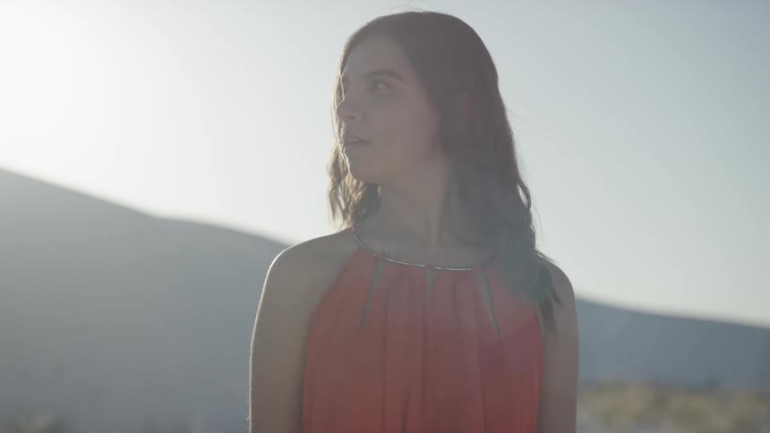A woman dressed in red turns her head and looks around on a sunny day