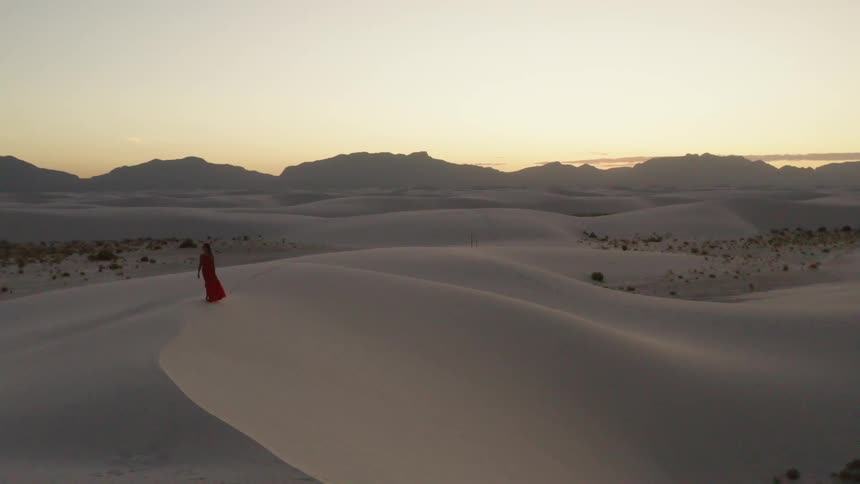 Aerial shot of a woman walking in a desert at dawn