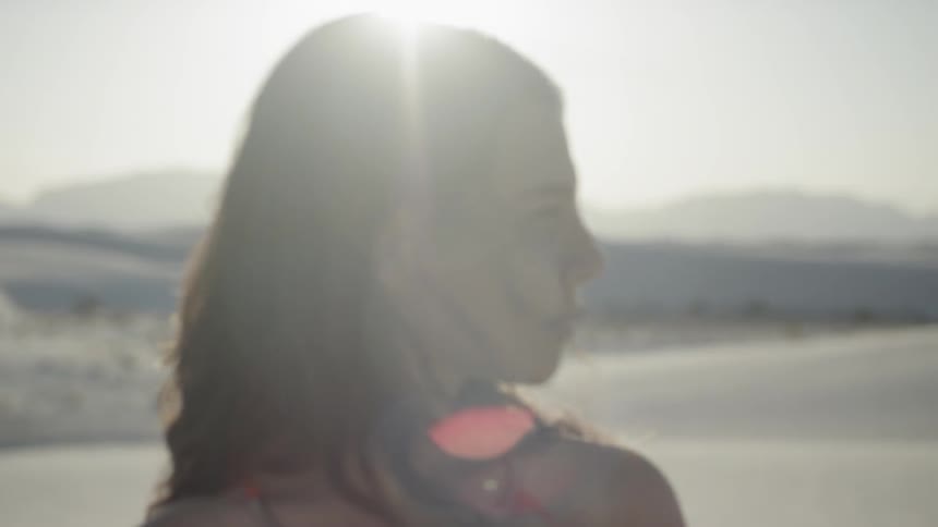 Brunette woman standing on the white sand desert looks around while the sun shines behind