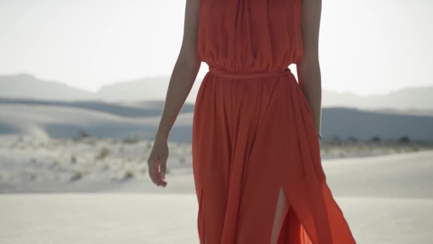 Woman in a long red dress walking barefoot on the sand in the desert