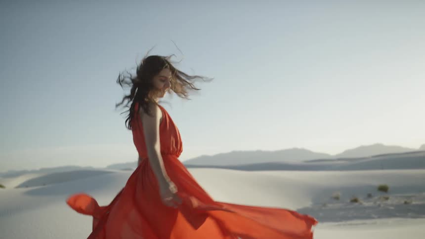 A white woman wearing an orange dress spins around in the desert