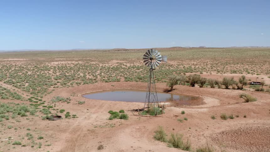 A windmill sits in front of a pond in a field