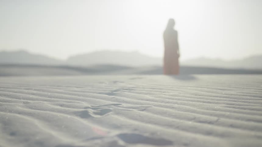 A woman in a red dress walking through the sand of a desert