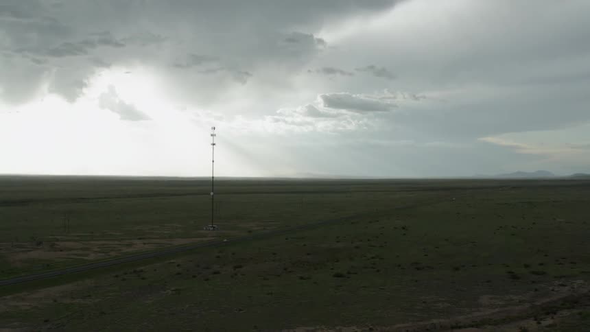 A cell phone tower or antenna in the middle of long stretch of land with a road down the center