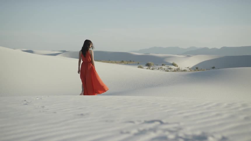 A woman in a red dress walks through the desert