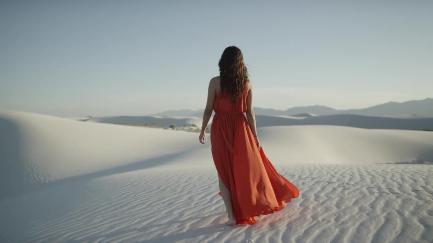 Woman in red dress walks across white desert sands