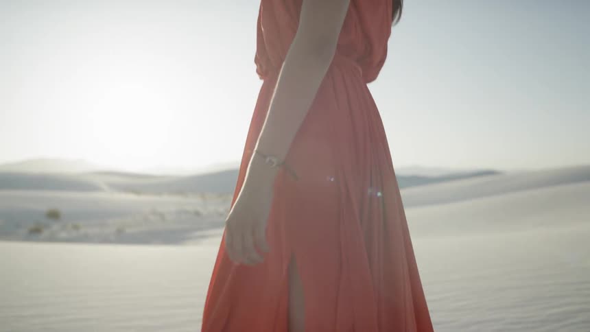 A young white woman wearing a gown wanders through a desert