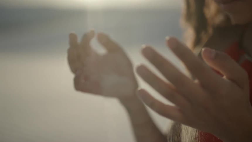 Brunette woman wearing a red dress slides the sand through her hands in the desert while the sun shines