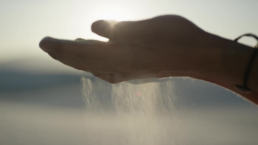 Sand trickles through cupped hands outdoors