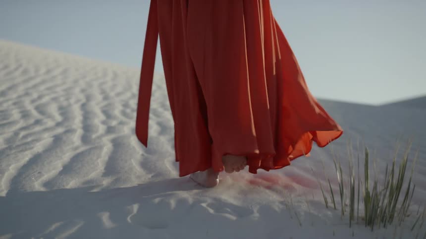 A woman in a dress walks up a sand dune
