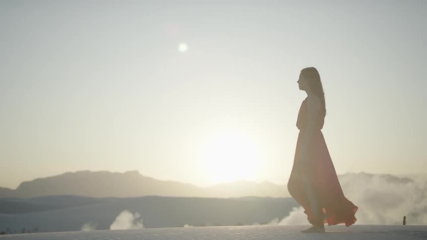 A woman in a red dress walking across the sand