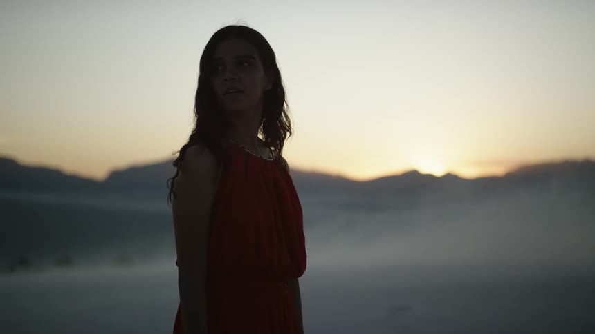 A woman is silhouetted against sky and mountains at sunset
