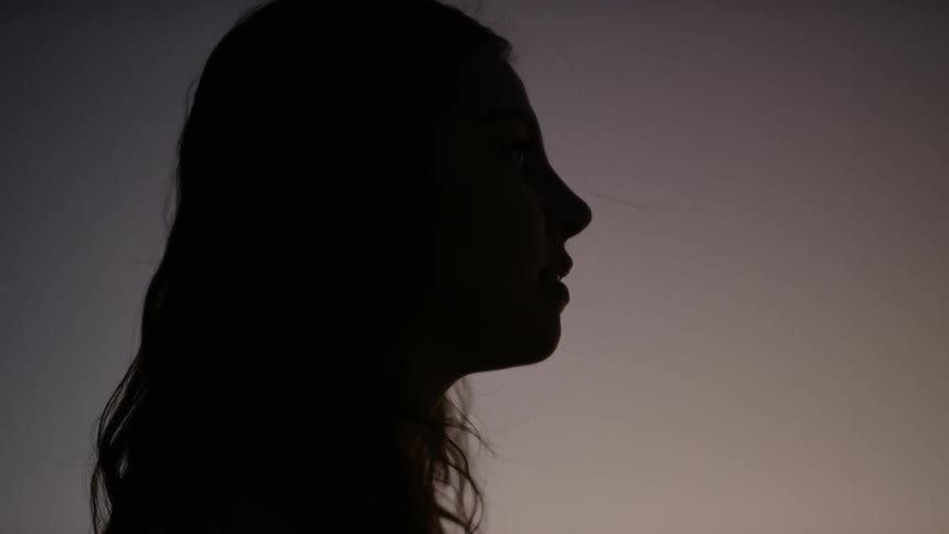 A woman outside with her hair blowing in the wind and the sky in the background
